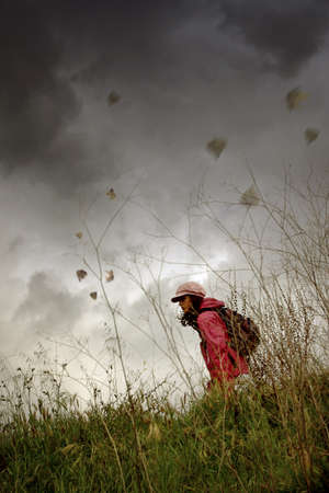 Young girl with hat and backpack walking alone in the countryside under bad weather