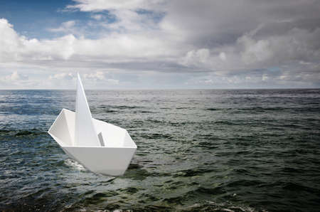 Single white paper boat adrift in the ocean under a stormy skyの写真素材