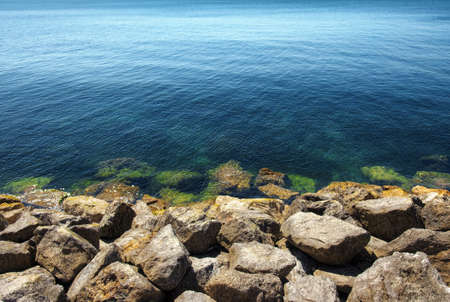 Seascape of calm blue ocean and rocky shore in the foreground
