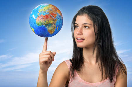 Pretty young brunette girl smiling and balancing a world globe in her fingerの写真素材