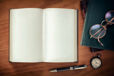 Open notebook, a pen and watch and a pair of glasses on top of booksの写真素材