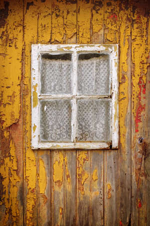 Detail of a weathered yellow wooden door with a small windowの写真素材