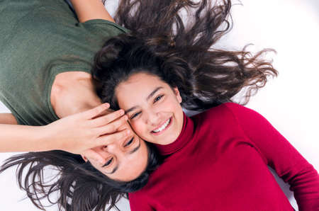 Two joyful teenager girl friends laying on the floor with their heads togetherの写真素材