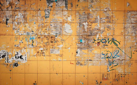 Yellow tiled wall with remains of ripped paper from advertising postersの写真素材