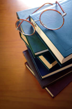 Pile of old books and a pair of vintage glasses on top of a table