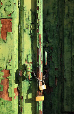 Old wooden door with green peeling paint and padlocksの写真素材