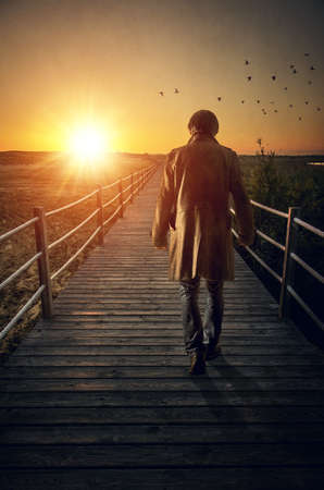 A man with long coat walking in a boardwalk into de sunsetの写真素材