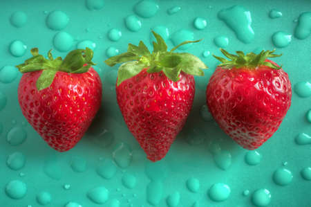 Three aligned strawberries over emerald green background with water dropsの写真素材