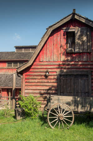 Red wooden western barn with a old wagon in foregroundの写真素材