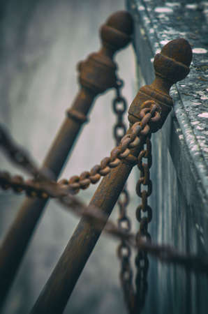 Fence with two iron poles and rusty chains bent against a stone wall