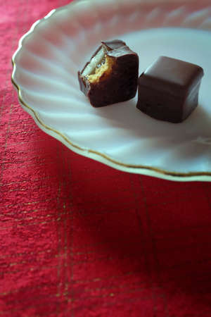 Two chocolates in a white glass plate over a red towel covering a table