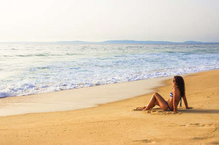 Single girl sitting in the golden sand by the sea shore in a summer dayの写真素材