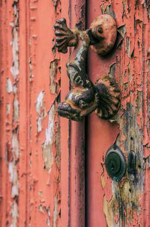 Fish shaped door knocker on an old wooden door with red peeling paintの写真素材