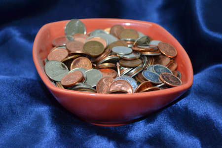 bowl of coins isolated on blue satin background