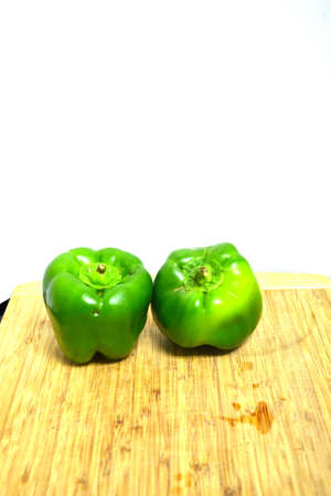 two green peppers on wood cutting board isolated on white backgroundの写真素材