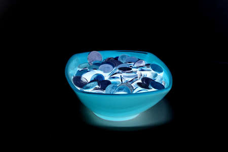 glowing bowl of coins isolated on black backgroundの写真素材