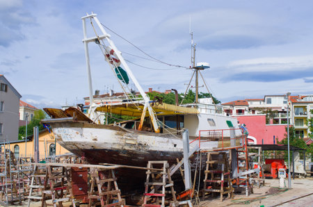 Seaside scene of a weathered fishing boat undergoing repair work on land. Great for illustrating industry, transport, construction, or travel themes.の写真素材