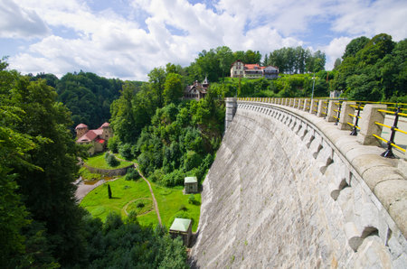Experience the grandeur of a massive concrete dam, nestled amidst vibrant green trees. A testament to engineering prowess, offering a scenic view of industrial power and natural beauty.の写真素材