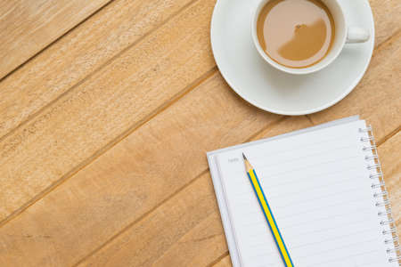 Top view of hot coffee on white cup and pencil on notebook on wood textures is diagonal for backgroundの写真素材
