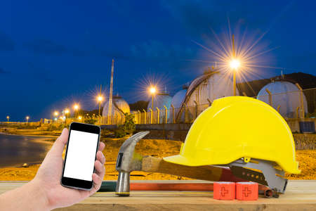 Front view of Hand holding the black smartphone and Yellow Safety Helmet, Hammer, Cutting tools on...