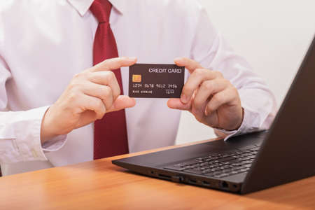 Close-up Of A Man's Two Hand Holding Credit Card on Front Of Laptopの写真素材