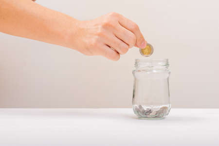 White hand man holding coin to putting in Jar or glass bottle for saving with soft white background. Saving money, Saving conceptの写真素材