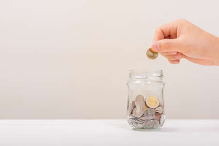 White hand man holding Gold coin to putting in Jar or glass bottle for saving with soft white background. Saving money, Saving conceptの写真素材