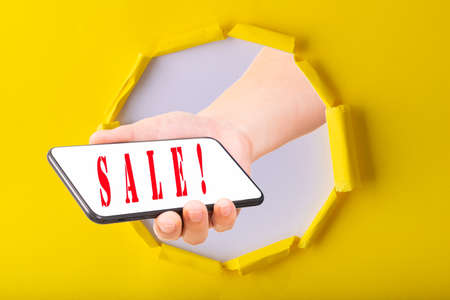 11.11 Single day sale. Hand hold smartphone through yellow paper torn with sale on screen smart...