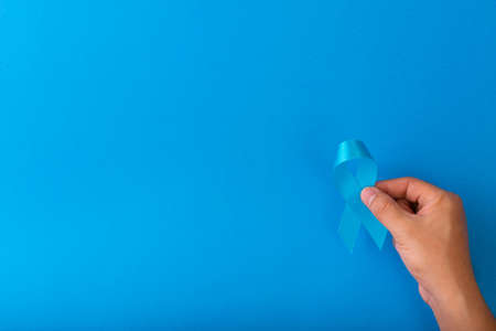 Blue ribbon awareness is being holding by hand isolated on blueの写真素材