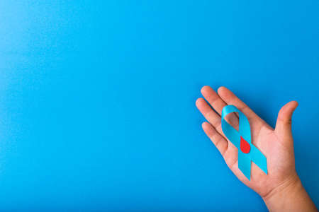 Blue ribbon awareness is being holding by hand isolated on a blue background with Copy space. World...