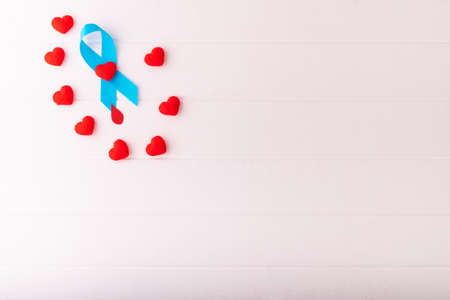 Blue ribbon awareness with red blood drop on a white wood background, many red heart around ribbon....