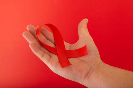 World AIDS day. Human hands holding red ribbon awareness on red background with copy space....