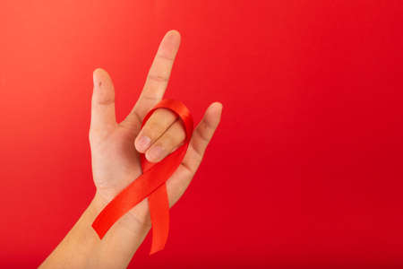World AIDS day. Human hands holding red ribbon awareness on red background with copy space. Healthcare concept.の写真素材