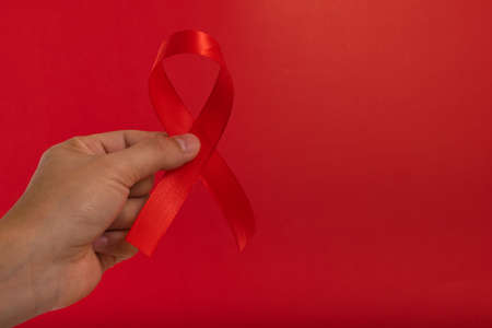 World AIDS day. Human hands holding red ribbon awareness on red background with copy space....