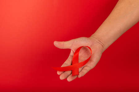 World AIDS day. Human hands holding red ribbon awareness on red background with copy space....