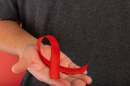 World AIDS day. Human hands holding red ribbon awareness on red background with copy space....