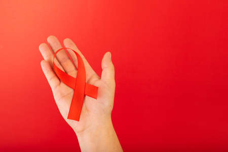 World AIDS day. Human hands holding red ribbon awareness on red background with copy space. Healthcare concept.の写真素材