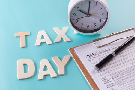 Tax fill concept - 'Tax day' word, clock, pen and calculator  with 1040 U.S. form on blue or green backgound colorの写真素材