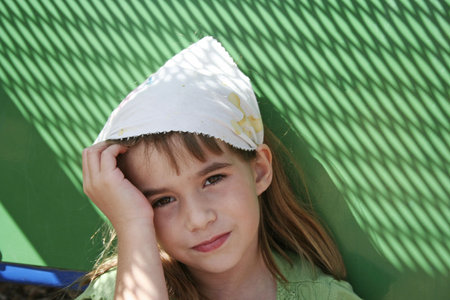 Sad little girl with green background wearing kerchief staring into cameraの写真素材