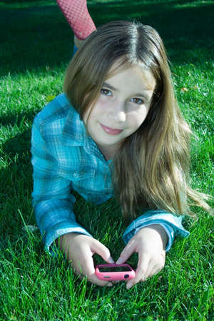 Pretty young girl holding cell phone laying on grassの写真素材
