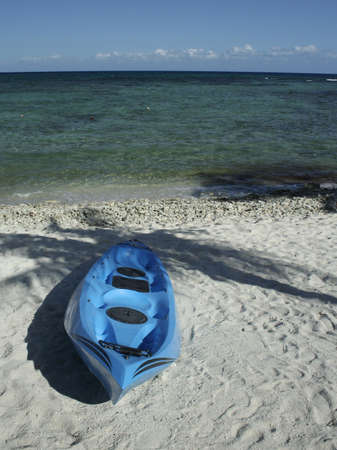 Blue kayak on sand of Mexican Caribbean beach with palm tree shadowの写真素材