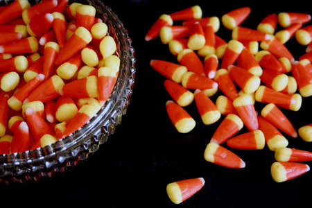 Candy corn in crystal bowl and scattered on black backgroundの写真素材