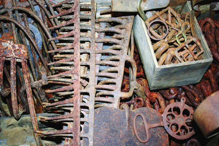 Assortment of rusted hand tools including rakes, pitchforks, and chainの写真素材