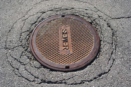 Rusted manhole sewer cover on cracked asphalt streetの写真素材