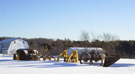 Snow covered antique farm equipment in morning sun with barnsの写真素材