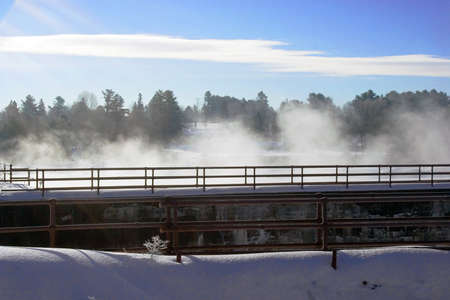 Winter river smoke rising to bridge walkwayの写真素材