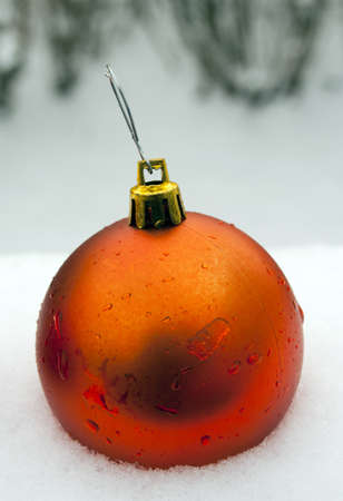 single orange christmas ornament in fresh snow with water dropletsの写真素材
