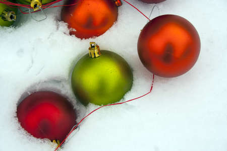 Red green and orange Christmas ornaments with raffia in fresh snowfallの写真素材