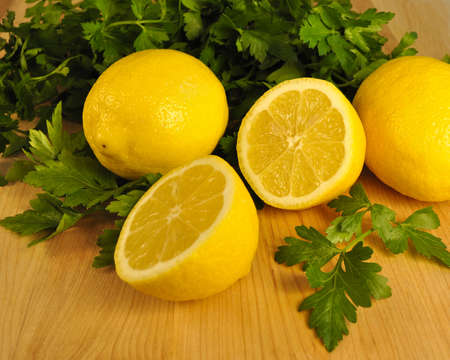 A horizontal shot of fresh cut lemons and flat leaf parsley on a wooden cutting board の写真素材
