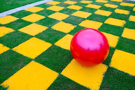 Vivid color of red ball lay on yellow tiles and fresh green field that look like chess grid.の写真素材